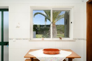 Ein Zimmer mit Fensterblick auf einen Garten, einem Holztisch mit Unterlage und einem Dekorationsgegenstand auf der Fensterbank.