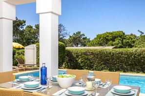 An outdoor dining area with a pool view, tables set with plates, glasses, and a blue bottle.