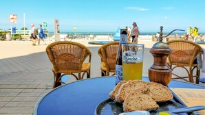 Ein Tisch mit einer Flasche Blanche de Narbonne, einem Glas Orangensaft und Brotscheiben auf einer blauen Tischdecke.