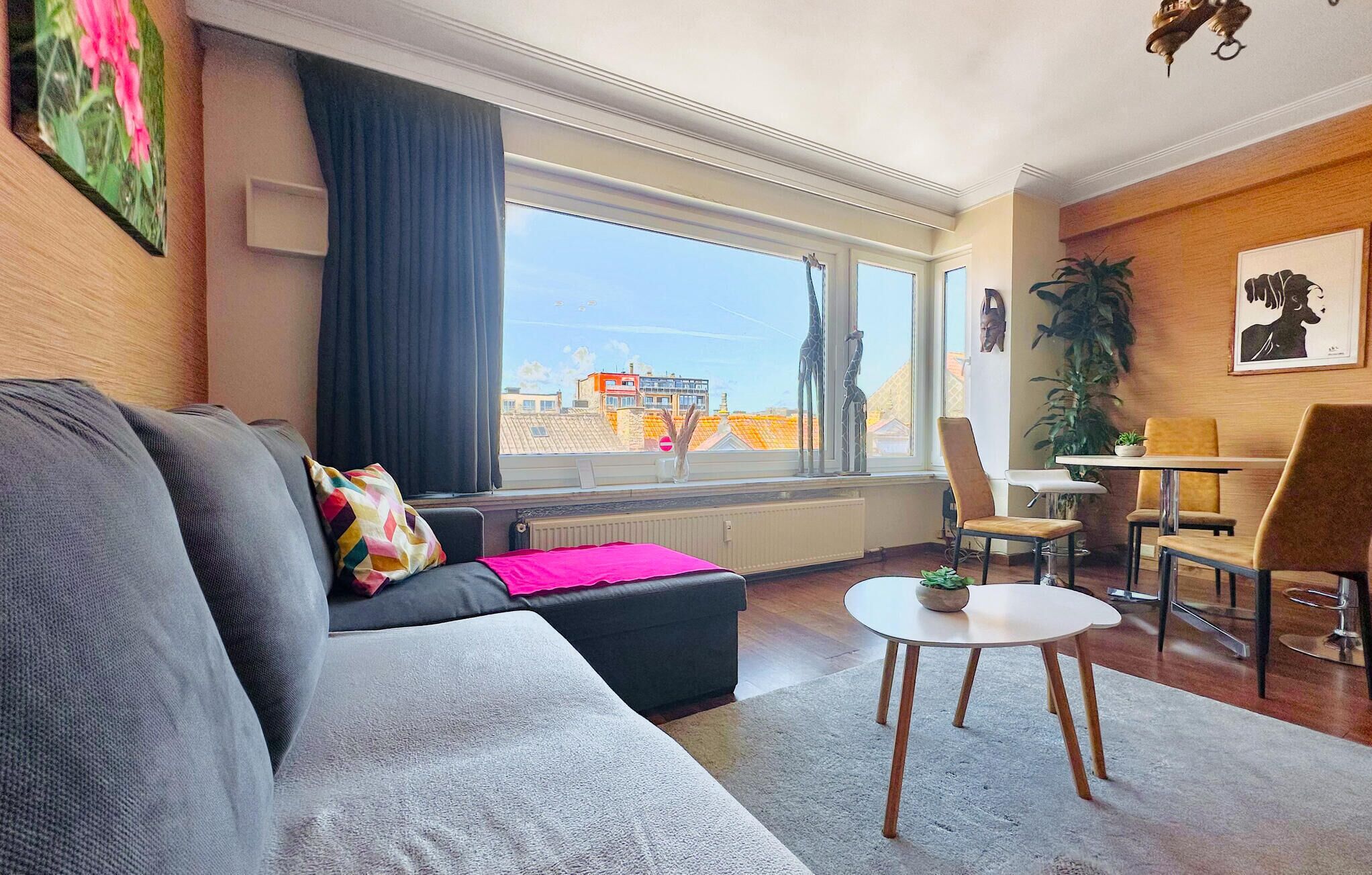 A modern living room with a grey sofa, a small round table, and a dining area with chairs.
