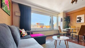 Ein modernes Wohnzimmer mit einem grauen Sofa, einem kleinen runden Tisch und einem Essbereich mit Stühlen.