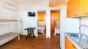 A compact room with bunk beds, a small table, a TV, and a kitchenette with orange cabinets. - sfinal residence (Peschici)