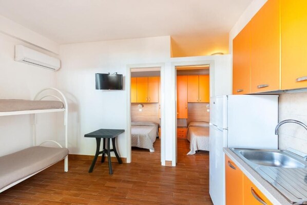 A compact room with bunk beds, a small table, a TV, and a kitchenette with orange cabinets. - sfinal residence (Peschici)