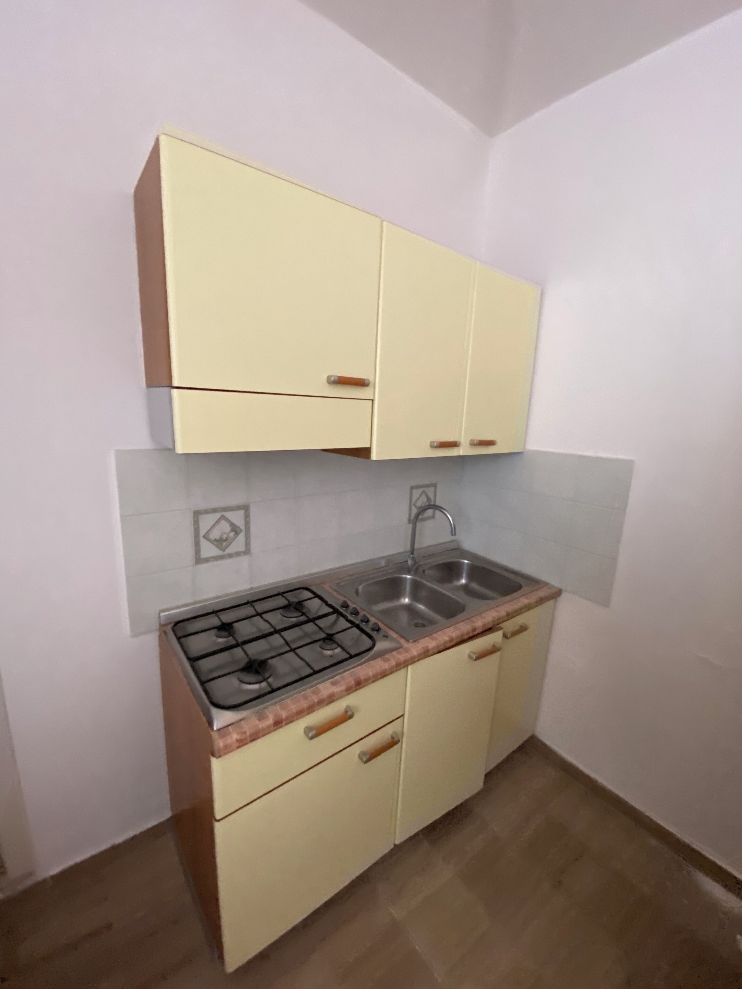 Een kleine keuken met een gasfornuis, twee spoelbakken en lichtgele kastjes.