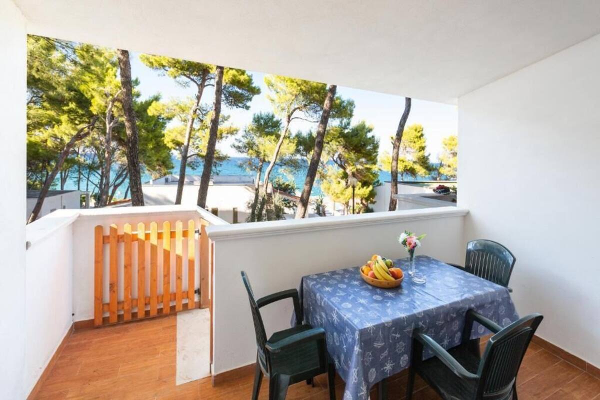 Un balcon avec une table et des chaises, donnant sur une zone côtière bordée d’arbres et offrant une vue sur la mer.