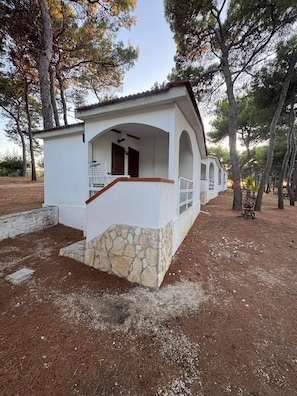 Un petit bâtiment d’un seul étage, avec une base en pierre et des murs blancs, doté d’un porche avec une balustrade et une porte.