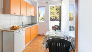 A compact kitchen with orange cabinets, a white countertop, and a dining area with a table and chairs. - sfinal residence (Peschici)