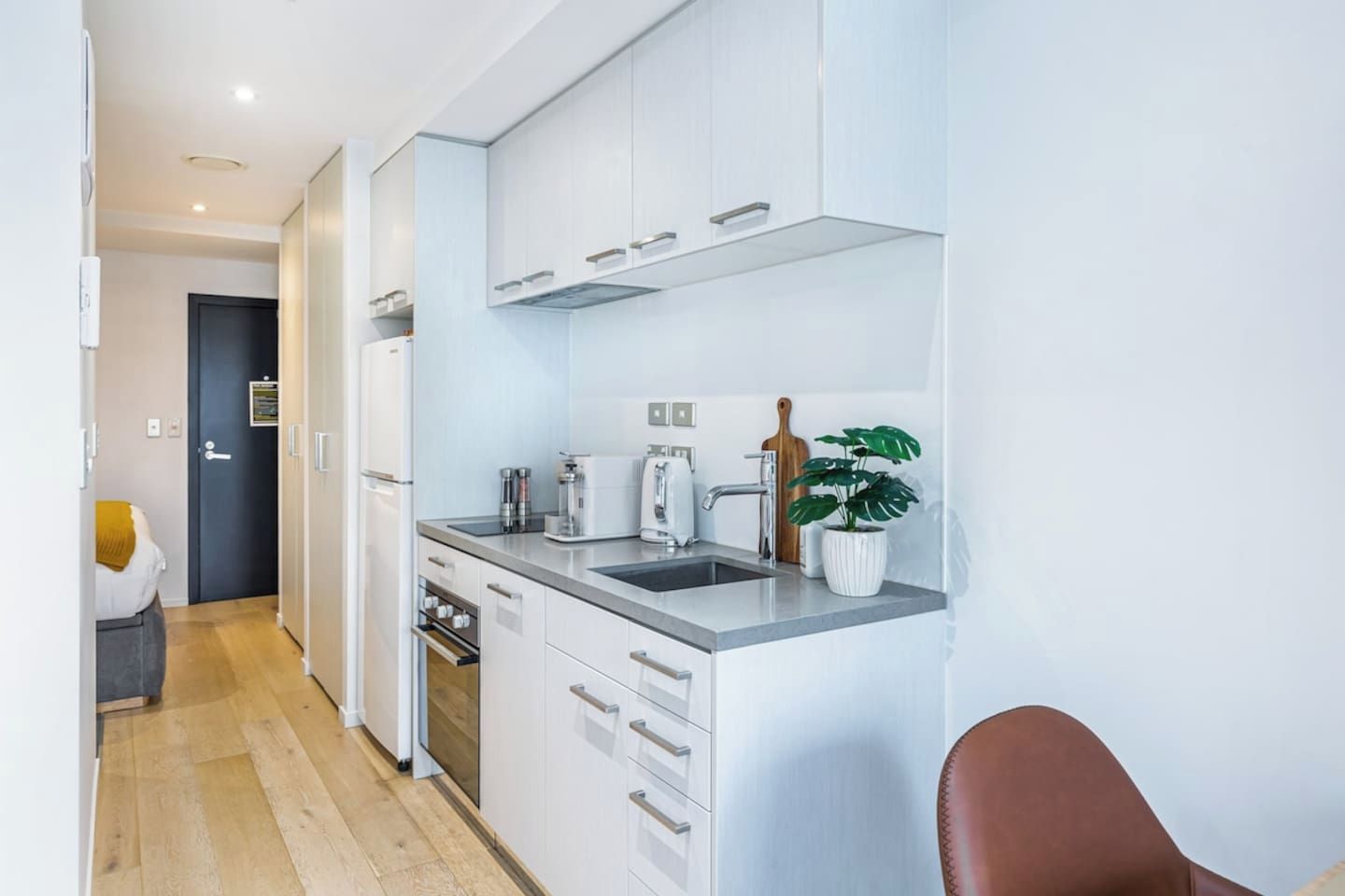 A modern kitchen with white cabinets, a stainless steel sink, and a countertop with a coffee maker and a potted plant.