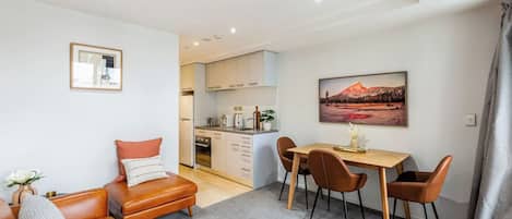 A modern living room with a brown leather sofa, a dining table with four chairs, and a kitchen in the background.