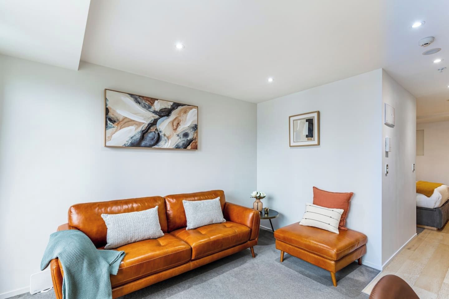 Un salon moderne avec un canapé en cuir, un fauteuil plus petit et une table basse. Un tableau est accroché au mur et une photographie encadrée se trouve au-dessus du fauteuil.