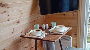 A wooden interior with a table set for two, a television mounted on the wall, and two metal stools.