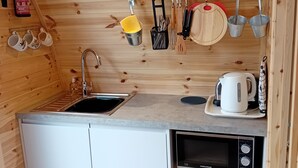 A compact kitchen with wooden walls, a sink, a microwave, and a small refrigerator.