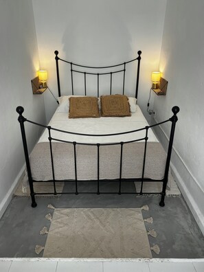 A bed with a metal frame, two pillows, a white mattress, and a beige rug. - Ibizan Style Studio in Jesus, Ibiza.  Peaceful yet centrally located. (Jesus)
