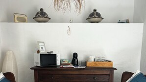 Ein Zimmer mit einem Holzkasten, zwei mit Kissen ausgestatteten Stühlen, einem Türkis-Teppich, einer Pendelleuchte und einer weißen Wand mit einem dekorativen Gegenstand.