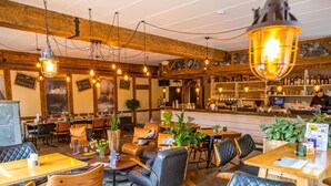 A cozy restaurant with wooden tables and leather chairs, a bar area with shelves of bottles, and hanging pendant lights. - Tent Lodge With Bathroom 16 km From Maastricht (Zutendaal)