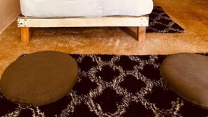 Un dormitorio con una cama, un tapiz de macramé, una lámpara colgante, una mesita de noche pequeña y una mesita auxiliar.