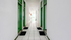 Un long couloir étroit, avec des portes vertes de chaque côté et un sol carrelé de carreaux blancs.