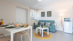 A modern living room with a sofa, a dining table with breakfast items, a lamp, and artwork on the wall.