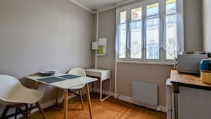 A small kitchen with a table and chairs, a radiator, and a window with lace curtains.