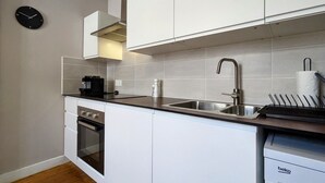 A modern kitchen with white cabinetry, a stainless steel sink, a built-in oven, and a coffee machine.