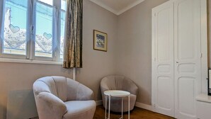 A room with a large window, a radiator, a white door, and two armchairs.