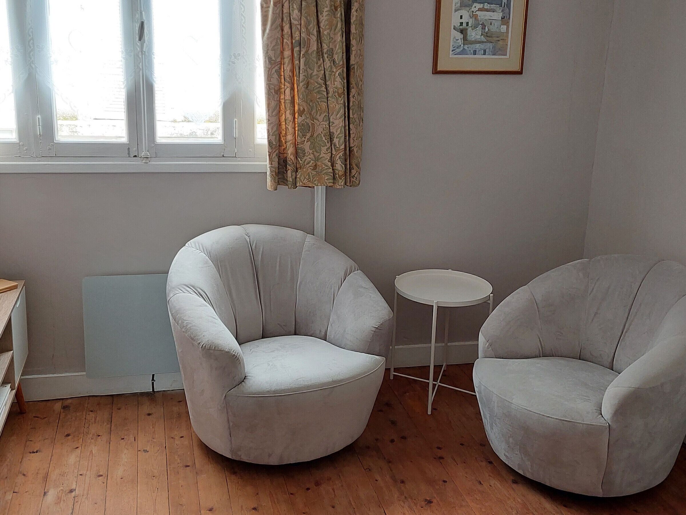 Een kamer met twee fauteuils, een klein rond tafeltje en een raam met gordijnen.