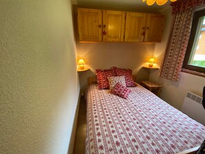 A small, cozy bedroom with a bed, two bedside lamps, and a window with curtains.