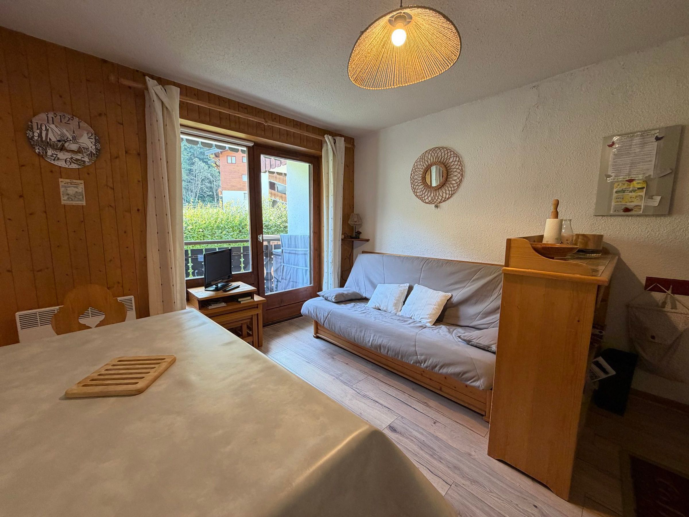 Une pièce comprenant un lit, une table, un téléviseur, un bureau en bois, une fenêtre avec des rideaux et une horloge murale.