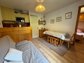 A cozy room with a bed, a dining table with benches, a kitchen area, and a wooden headboard.