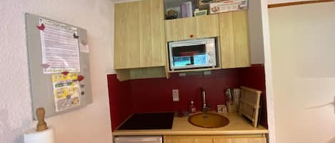 A compact kitchen with a microwave, sink, and wooden cabinets.