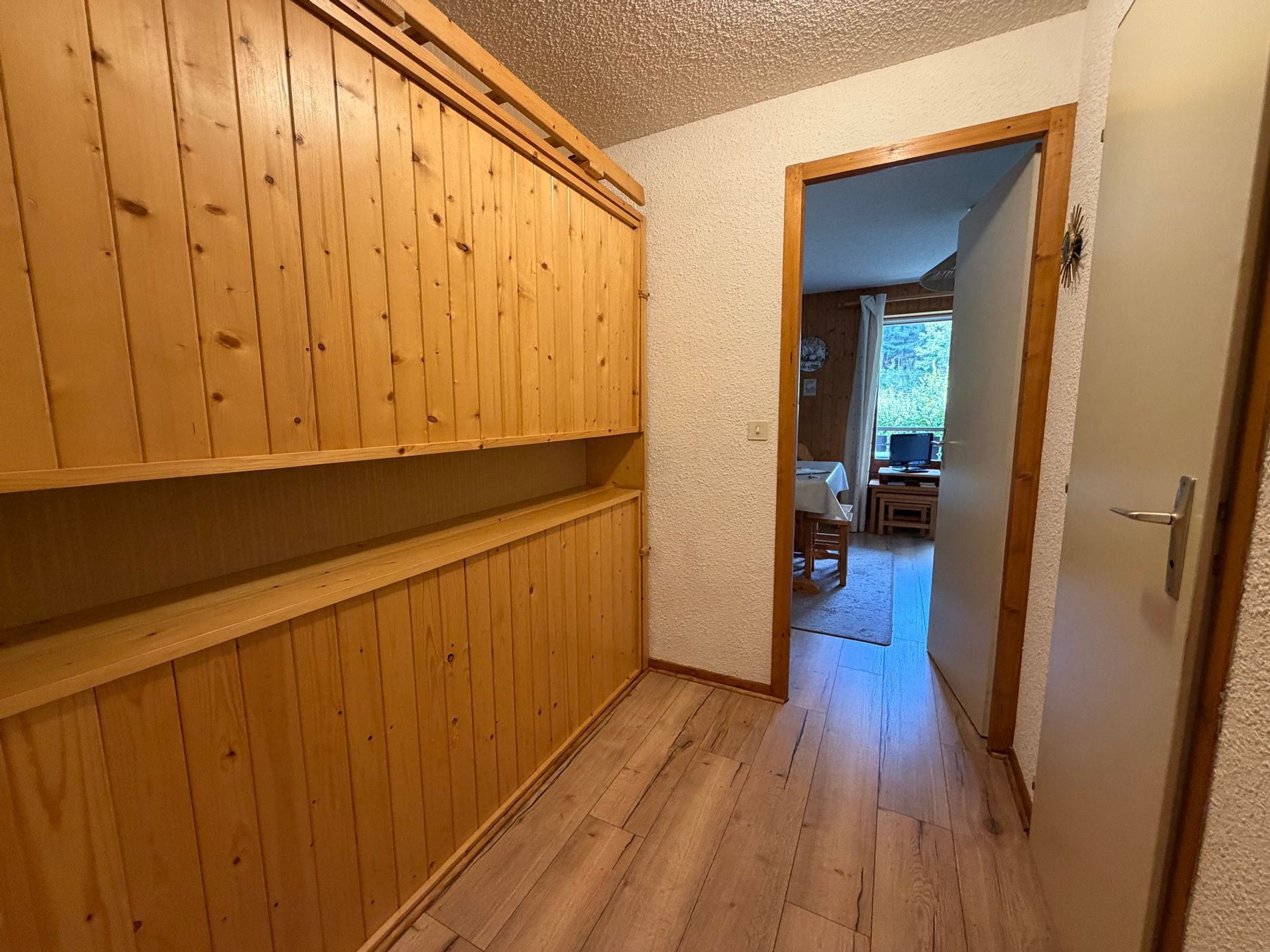 En gang med træpaneler og en dør, der fører til et spiseområde med et bord og stole.