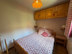 A bedroom with a bed, wooden cabinets, a nightstand, and a hanging lamp.