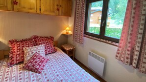 A bedroom with a bed, wooden cabinets, a window with curtains, a bedside table with a lamp, and a radiator. - Châtel: 2-Room Apartment, Balcony, Parking, WIFI, Pets OK (Châtel)