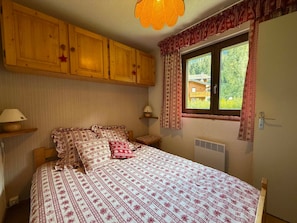 Ein Schlafzimmer mit einem Bett, Holzschränken, einem Fenster mit Vorhängen und einer Wandlampe.