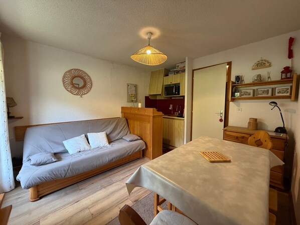 A compact living space with a sofa, a dining table, a kitchen area, and a mirror.