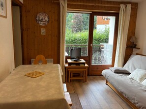 A room with a bed, a table with a tray, a television on a small table, and a window with a view of greenery.