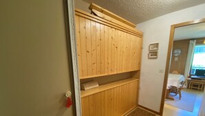 A wooden cabinet with shelves, a small rug, and a door with a red handle. - Châtel: 2-Room Apartment, Balcony, Parking, WIFI, Pets OK (Châtel)