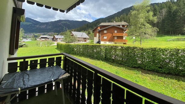 A balcony with a view of a wooden house and mountains in the background. - Châtel: 2-Room Apartment, Balcony, Parking, WIFI, Pets OK (Châtel)