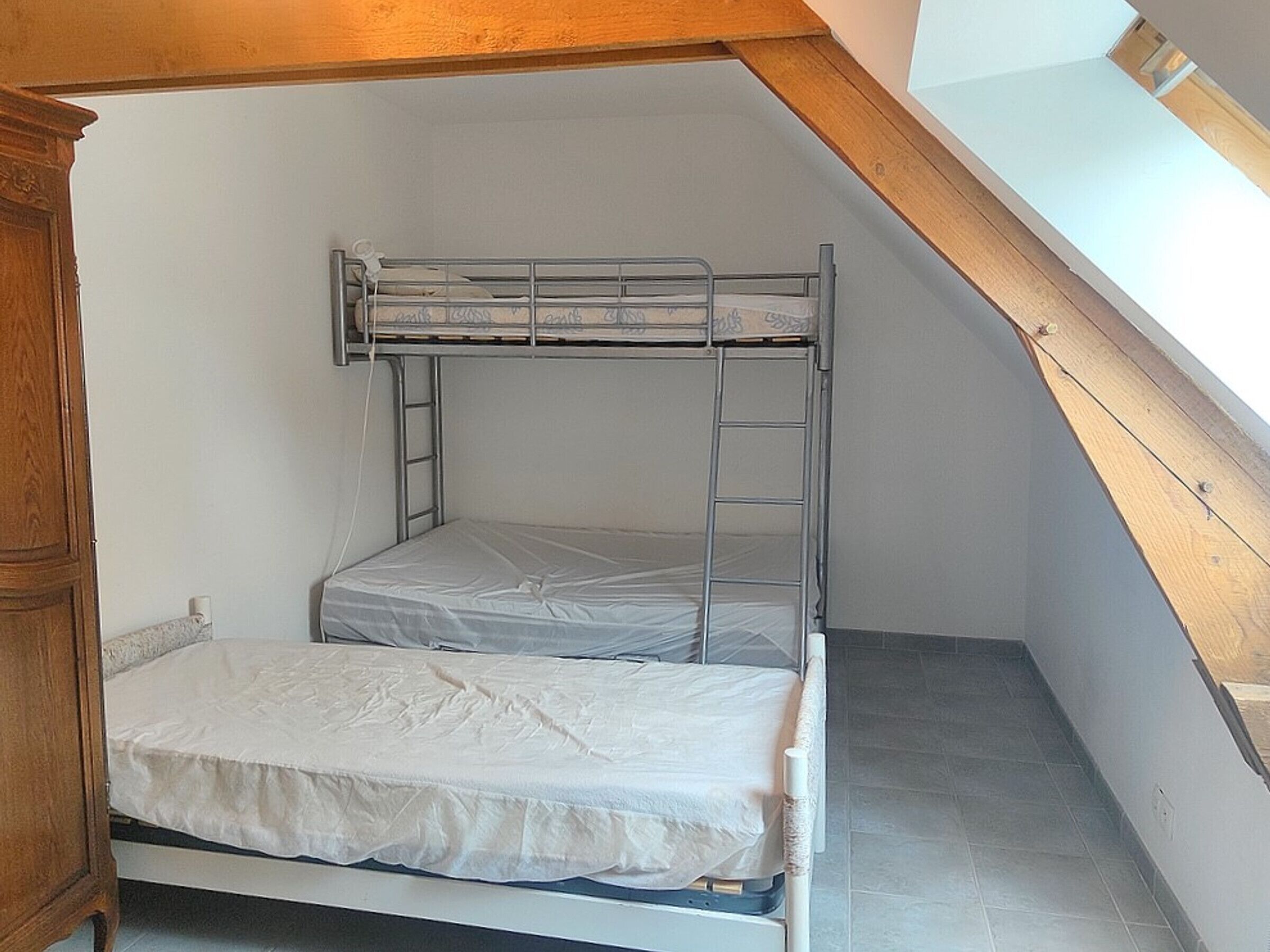 Une chambre de type dortoir, avec un lit superposé, une armoire en bois et un plafond en pente doté d’un puits de lumière.