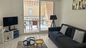 A modern living room with a flat-screen TV, a sofa, a small table, and a balcony with a table and chairs.