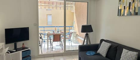 A modern living room with a flat-screen TV, a sofa, a small table, and a balcony with a table and chairs.