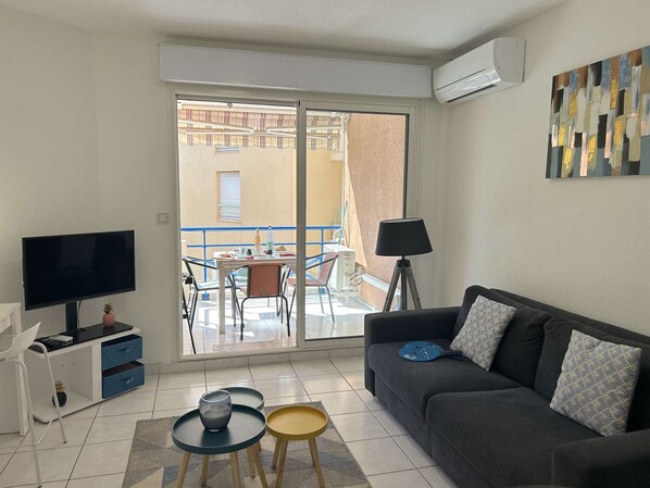 Un salon moderne doté d’un téléviseur à écran plat, d’un canapé, d’une petite table et d’un balcon avec une table et des chaises.