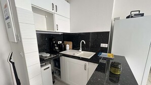 A compact kitchen with white cabinets, a black countertop, a sink, and a refrigerator.