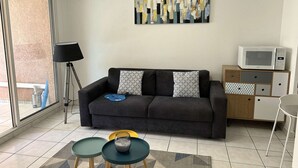 A living room with a sofa, two side tables, a lamp, a microwave, and a TV on a cabinet.