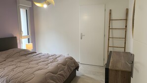 Quarto com cama, luminária, porta e escada de madeira encostada na parede.