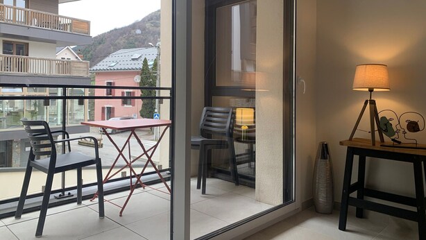 Uma varanda com mesa e cadeiras, um candeeiro e vista para um edifício e colinas ao fundo.
