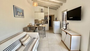 Un espace de vie compact comprenant un coin cuisine, un coin repas et un téléviseur fixé au mur.