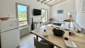 Une cuisine compacte équipée d’un réfrigérateur, d’une table à manger avec des chaises, d’un téléviseur et d’une fenêtre donnant sur un espace verdoyant.