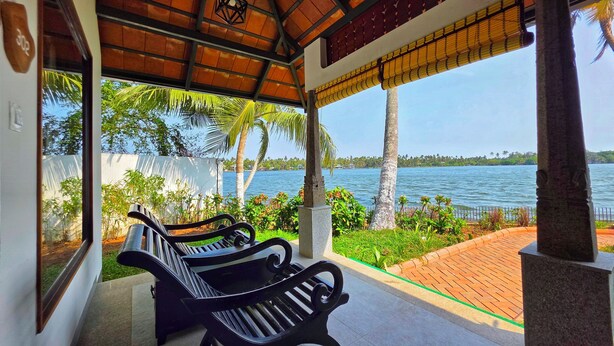 A covered seating area with benches, a view of a lake, and palm trees. - Vedic Village Retreat (Kodungallur)