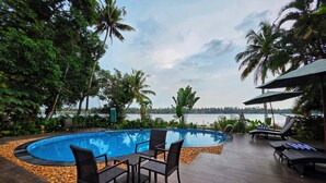 A swimming pool with lounge chairs and a view of the sea. - Vedic Village Retreat (Kodungallur)